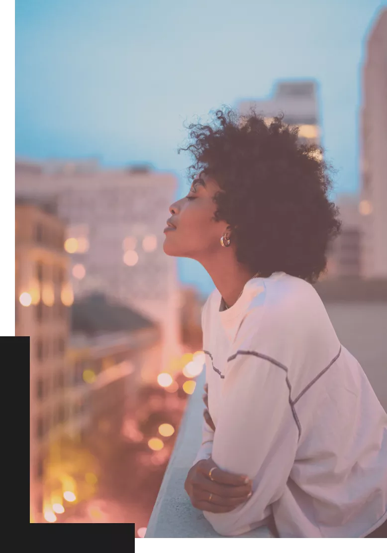 Black woman with long curly hair and white blouse looking into the distance on a rooftop